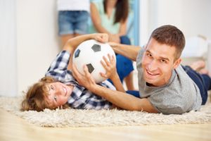 Glücklicher Vater und Junge spielen und toben mit Fußball im Wohnzimmer