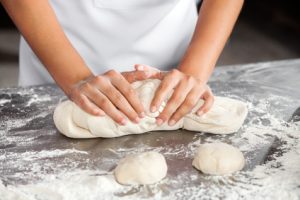 Midsection of female baker kneading dough at table in bakery