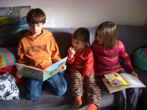 drei Kinder sitzen am Sofa und lesen 