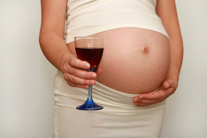 Schwangere Frau hält Rotweinglas vor ihrem Bauch.